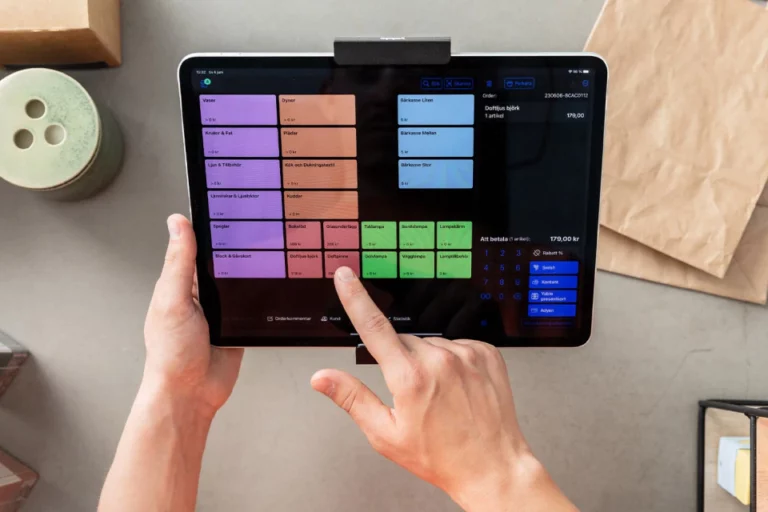Användarens händer interagerar med en Yabie kassasystemapplikation på en surfplatta, som visar ett färgglatt gränssnitt med olika affärskategorier.